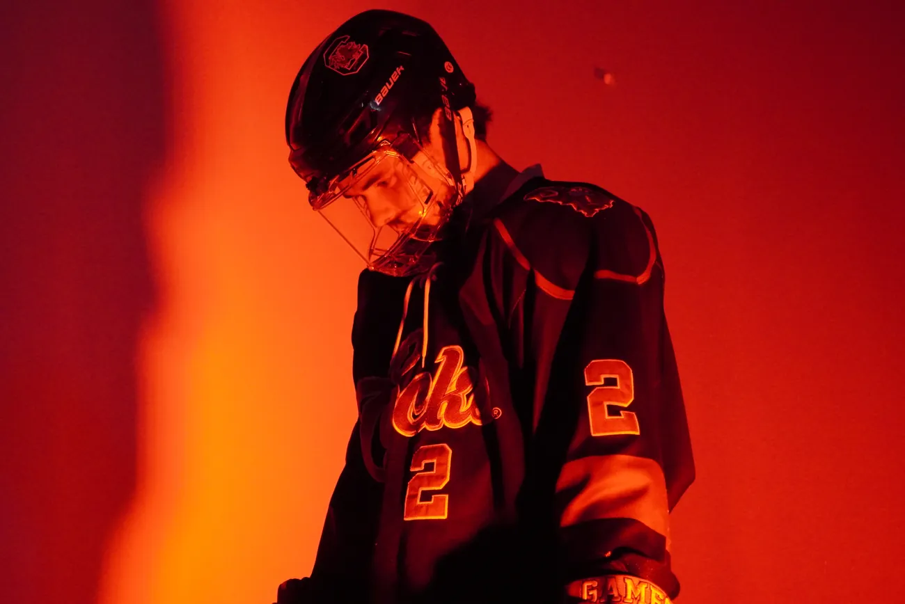 Gamecocks player number 2 with his head bowed, his cage lit from the side against deep red light