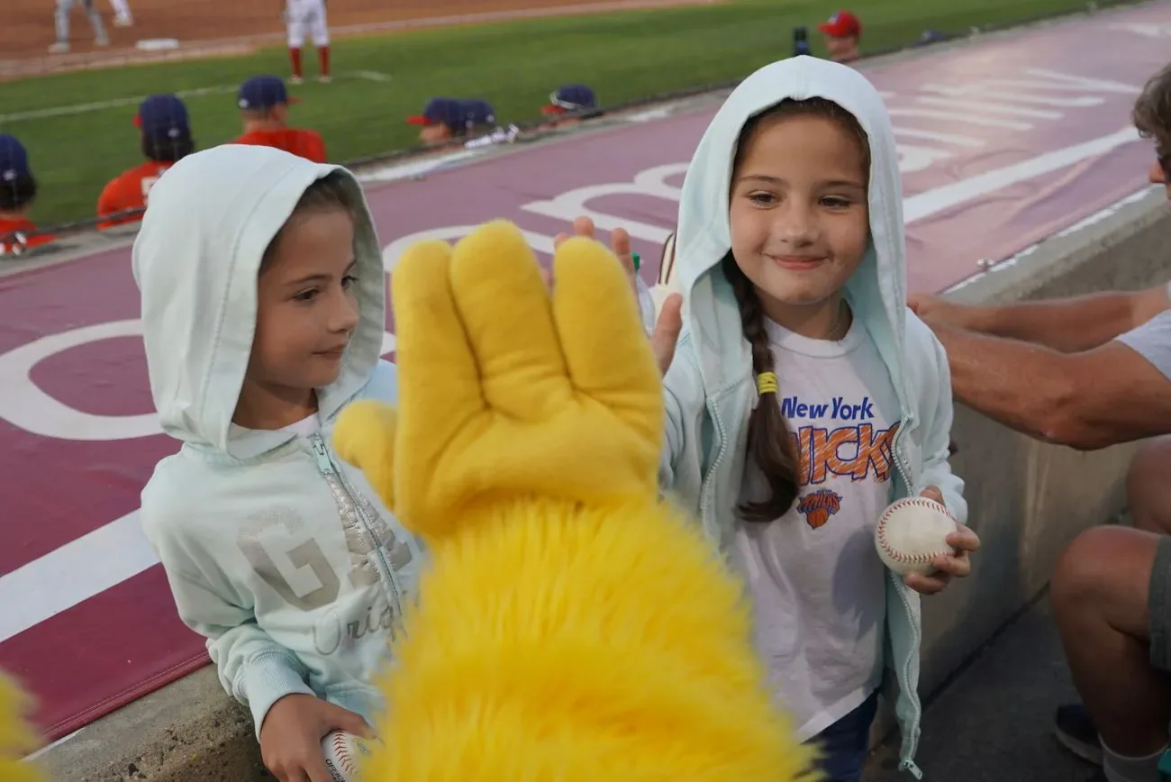 Two kids in rain ponchos holding baseballs and high-fiving Buster's glove