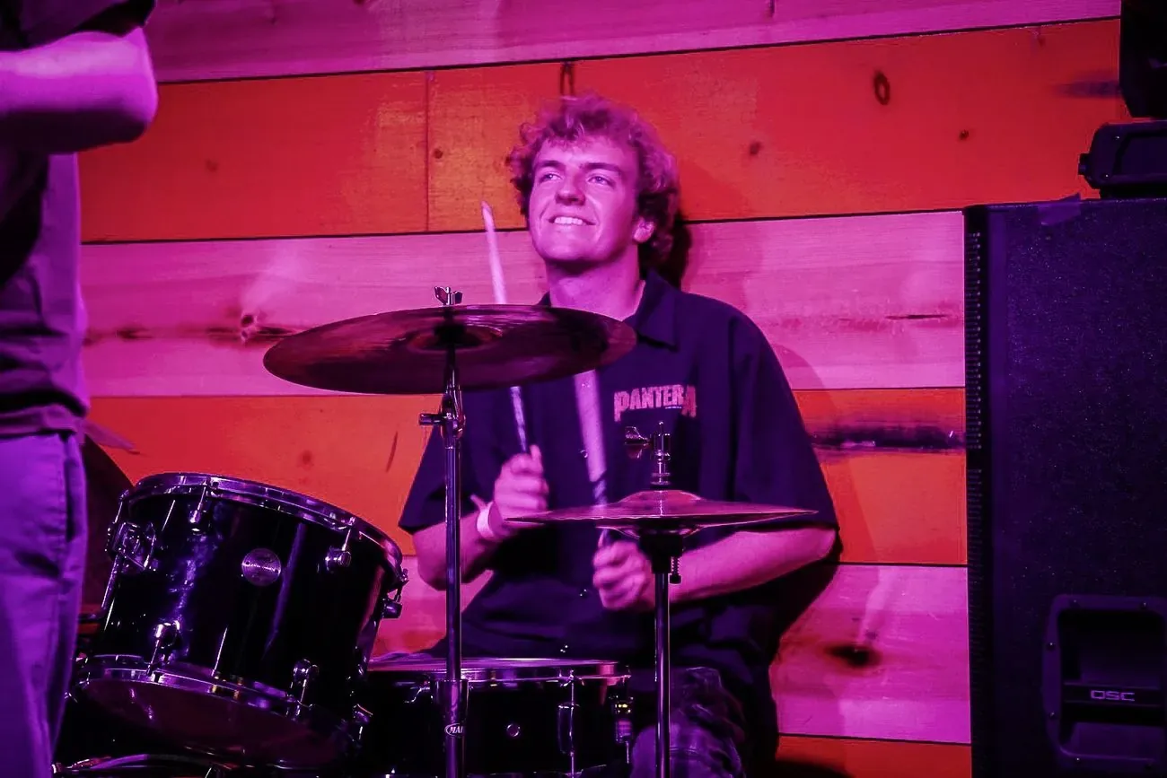 Drummer mid-song lit in pink and purple stage light