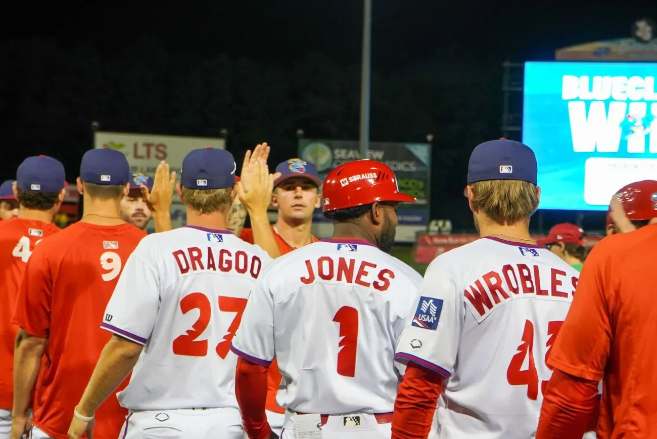 BlueClaws players high-fiving down the line after a win as the video board reads BlueClaws Win