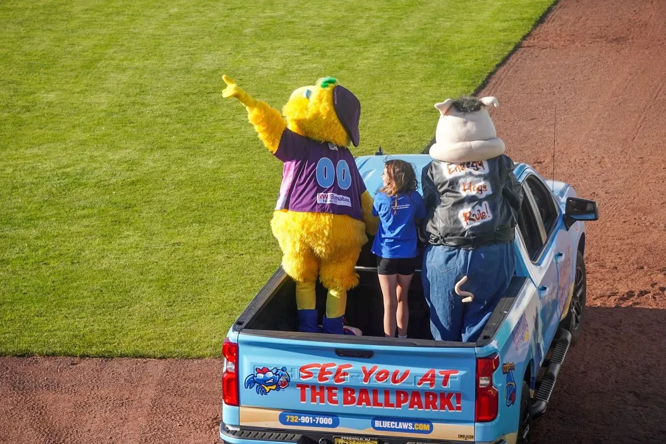 Buster riding in the bed of a pickup with a See You at the Ballpark sign