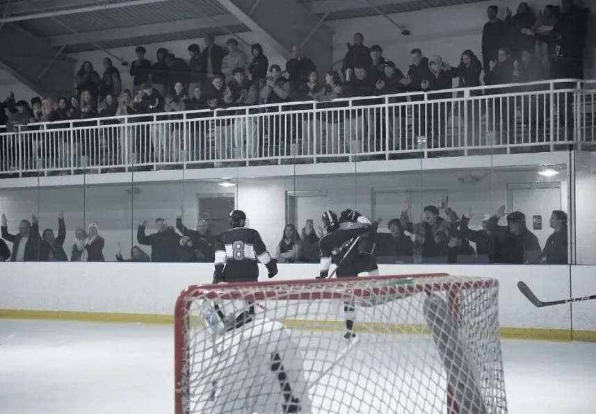 Black and white frame of a packed rink balcony of standing fans above an empty net