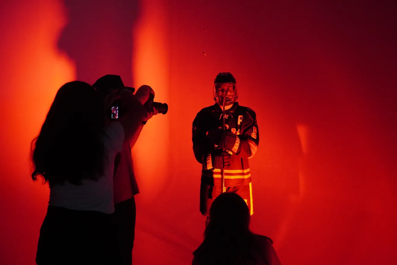 Two photographers working a Gamecocks player against the red backdrop on media day