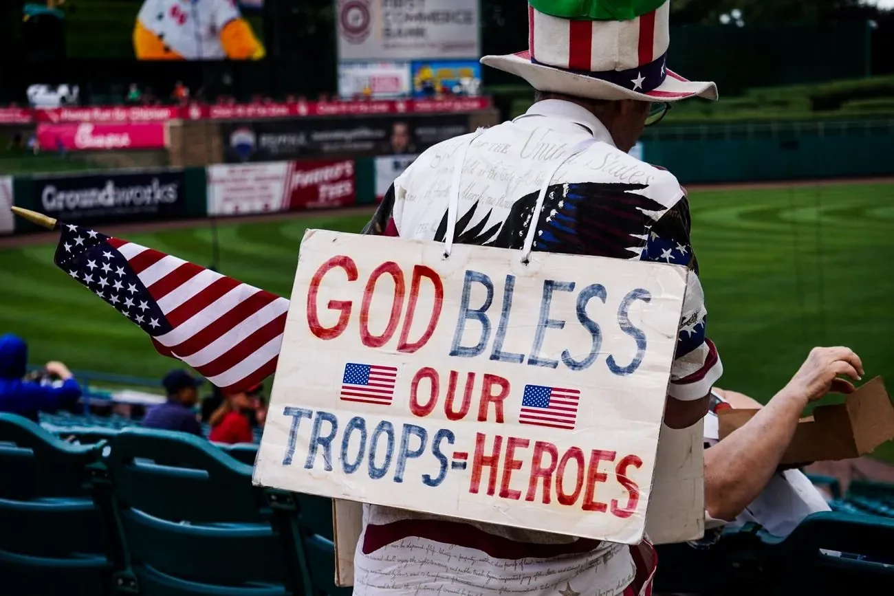 Fan in a stars and stripes outfit holding a hand-painted God Bless Our Troops sign