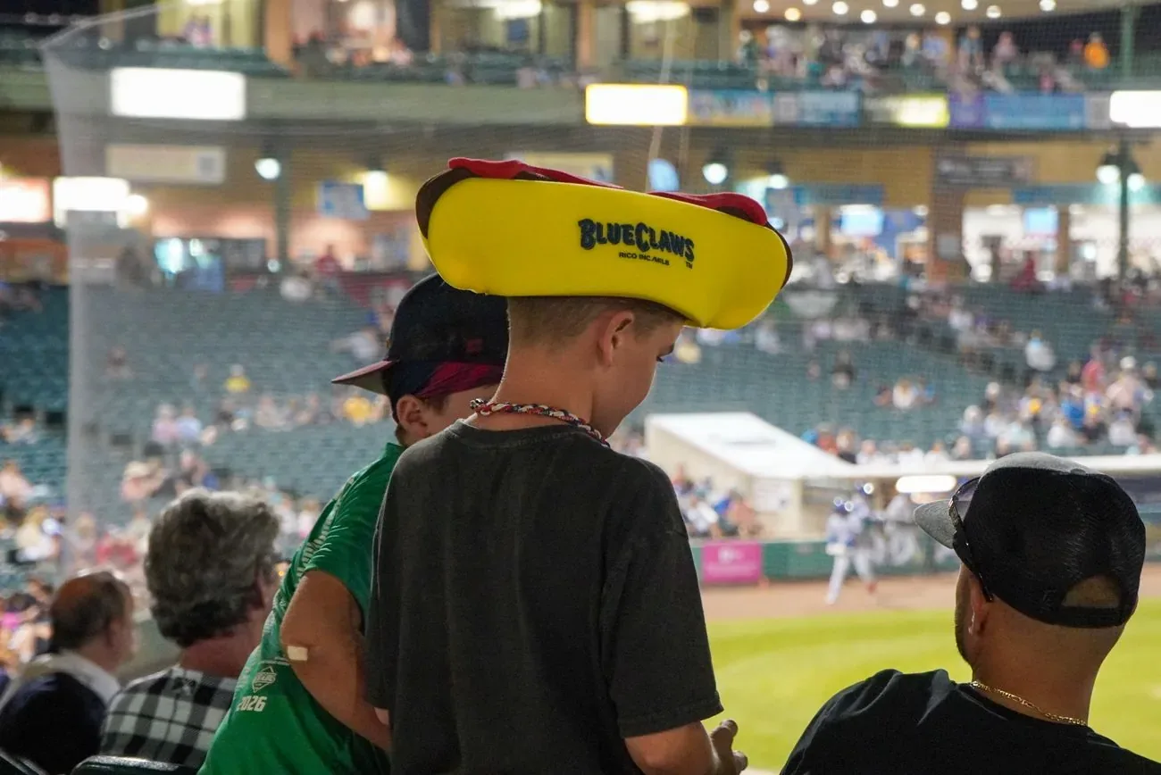 Young fan wearing a foam BlueClaws hot dog hat in the stands