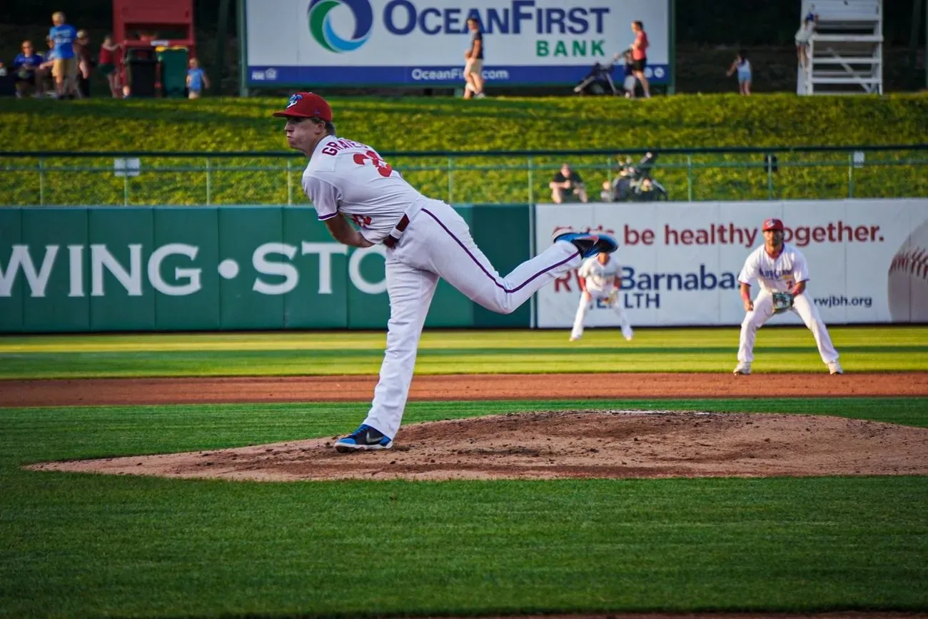 BlueClaws pitcher at the top of his delivery on the mound, outfield signage behind him