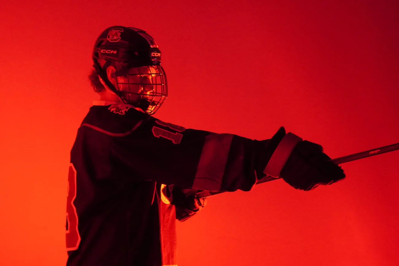 Gamecocks player in profile extending his stick out to one side, rim lit in red