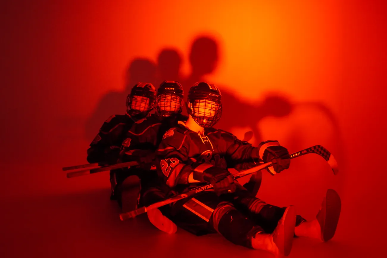 Three Gamecocks players seated in a stacked row on the floor with their sticks across their laps