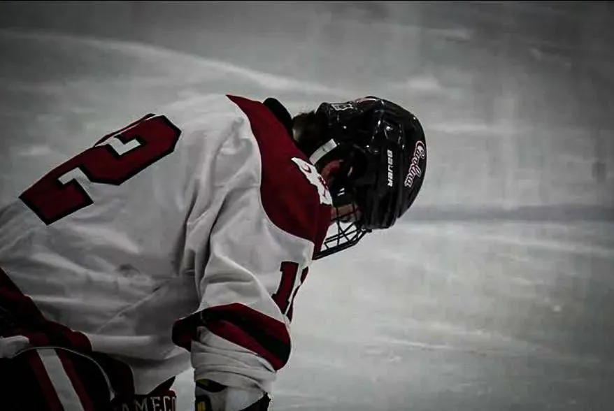 Player in a white Gamecocks jersey with his head down, catching his breath on the ice