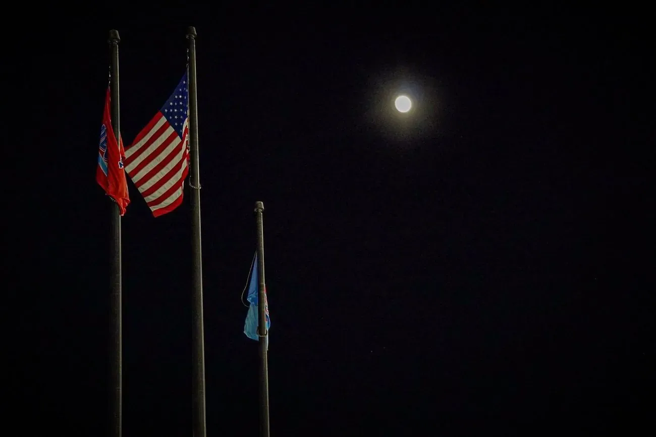 Full moon above three flagpoles against a black night sky