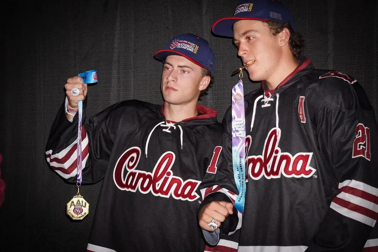 Two Carolina players in black jerseys after the title game, one holding up a gold medal