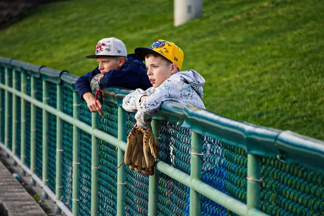 Two young fans in team caps leaning over the outfield rail with a baseball glove