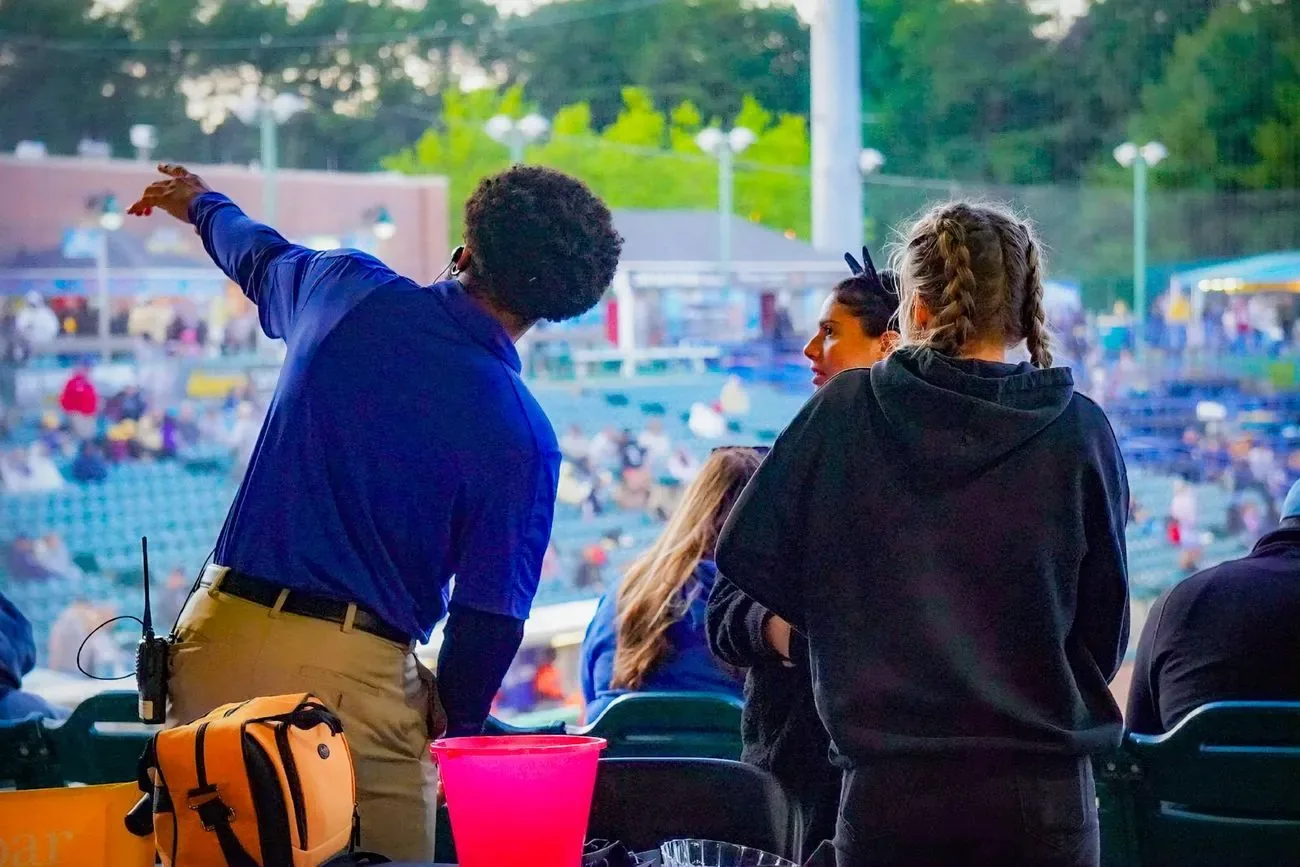 Gameday staffer in a blue polo pointing out a seat location to fans in the stands