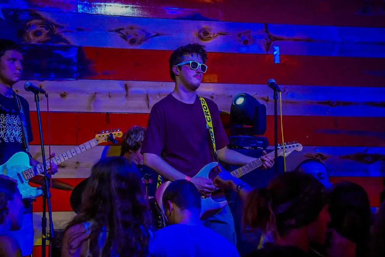 Guitarist in sunglasses playing under red and blue stage lights