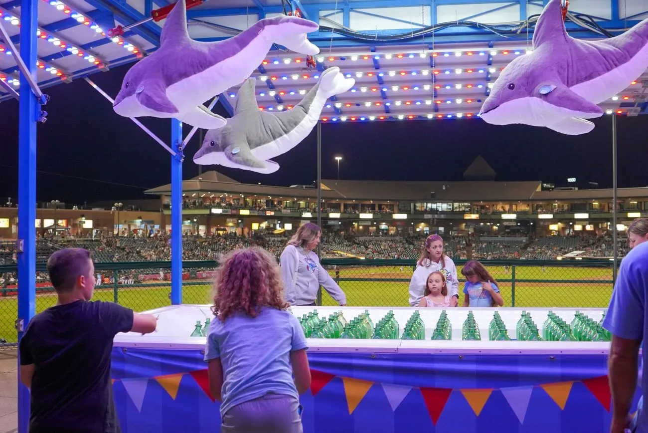 Kids playing a boardwalk carnival game with inflatable dolphins strung overhead