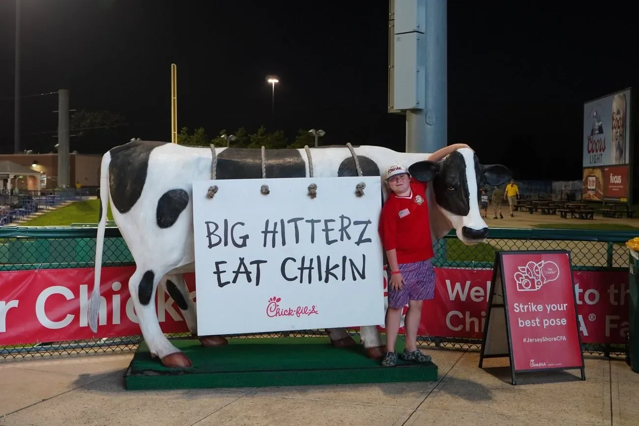 Chick-fil-A cow cutout with a hand-lettered Big Hitterz Eat Chikin sign at a sponsor activation